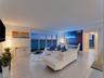 Floor-to-ceiling glass sliding doors opening to a balcony, ceramic tile flooring, accent wall, and expansive coastal horizon