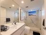Modern floating vanity with an integrated rectangular sink and chrome faucet, floor-to-ceiling vanity mirror, walk-in shower with stone-look wall pane