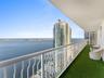 Private balcony featuring a synthetic turf floor, white metal railing, and extensive water and city skyline surroundings
