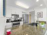 Kitchen featuring stone countertops, stainless steel appliances, white cabinetry, a single-basin undermount sink, and a high-arch pull-down faucet
