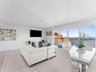 Open-concept area featuring oversized windows, floor-to-ceiling glass sliding doors, neutral ceramic tile flooring, and a metal-railing balcony