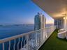 Covered balcony with white metal railings, synthetic turf flooring, and attached wall-mounted lighting
