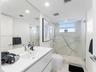 Modern floating vanity with an integrated basin, expansive wall-to-wall mirror, glass-enclosed shower with stone-vein tile surround, and recessed ceil