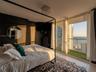 Floor-to-ceiling glass walls, private balcony with synthetic turf surfacing, square crystal flush-mount light fixture, and circular wall-mounted mirro