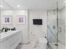 Floating white vanity with integrated sink, glass-enclosed walk-in shower with stone-style wall tile, large frameless wall mirror, and recessed lighti