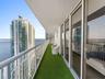 Covered balcony featuring white metal railings, synthetic turf flooring, and sliding glass door access