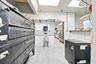 Commercial kitchen workspace featuring a multi-deck industrial oven, stainless steel hand sink, tiled wall finishes, and integrated refrigeration unit