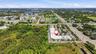 Aerial perspective featuring a commercial structure with a flat roof, asphalt surface parking, expansive paved access, and proximity to major arterial
