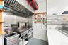 Commercial kitchen space featuring stainless steel wall cladding, professional-grade ventilation hood, built-in flat-top grill, deep fryer, and white 