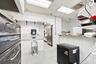 Commercial kitchen workspace featuring tiled wall finishes, a stainless steel basin, dual-door refrigeration unit, and a stone-surface service counter