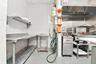 Commercial kitchen space featuring stainless steel preparation counters, wall-mounted shelving, a professional-grade stainless steel exhaust hood, and