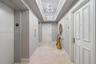 Hallway featuring stone tile flooring, crown molding, dual crystal chandelier light fixtures set within a tray ceiling, and panel-style entry doors