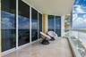 Covered balcony featuring stone tile flooring, floor-to-ceiling glass sliding doors, and a transparent glass pane railing
