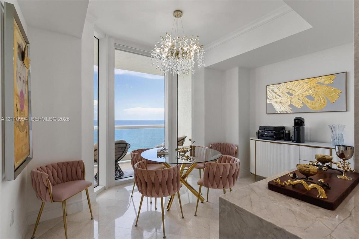 Dining area featuring large-format polished stone flooring, floor-to-ceiling windows with ocean horizon, a multi-tiered crystal chandelier, and built-