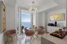 Dining area featuring large-format polished stone flooring, floor-to-ceiling windows with ocean horizon, a multi-tiered crystal chandelier, and built-