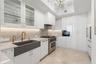Kitchen featuring high-gloss cabinetry, stone-finish countertops, a dark-toned apron-front sink with gold-tone fixtures, stainless steel professional-