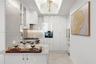 High-gloss white cabinetry featuring polished hardware, stone-finish countertops, recessed tray ceiling with crystal-style chandelier, and built-in st