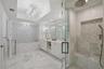 Bathroom featuring a white double-vanity, walk-in glass-enclosed shower with a built-in bench, soaking tub with decorative tile surround, and crystal 