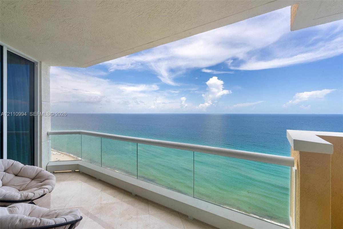 Covered balcony featuring tile flooring and a glass panel railing with a horizontal metal top rail