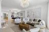 Open-concept interior featuring large-format polished stone flooring, crown molding, and dual ornate crystal chandeliers