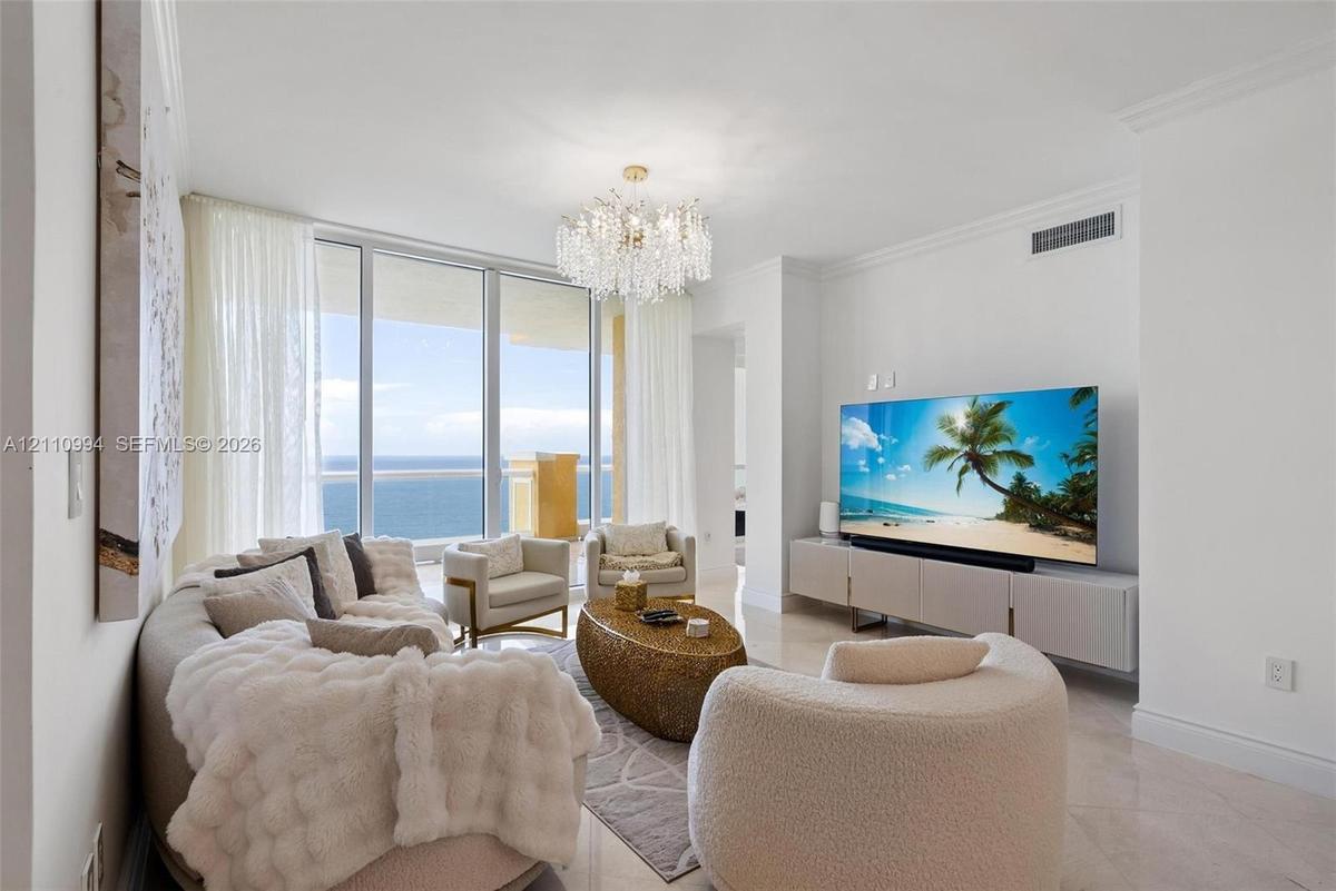 Living space featuring floor-to-ceiling glass panel doors, polished stone flooring, a multi-tiered crystal chandelier, and crown molding