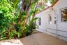 Exterior wood decking featuring a stucco facade, tile roof edging, and mature tropical landscaping