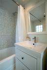 Bathroom featuring speckled stone-finish wall tile, a glass block window, a white vanity with a rectangular sink, a polished metal faucet, and a wall-
