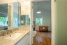 Bathroom featuring a white undermount sink, stone-finish countertop, full-width mirror, and satin-finish metal fixtures, with a wood-finish floor and 