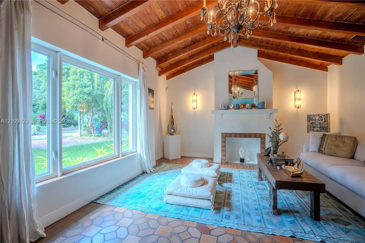 Vaulted ceiling with exposed wood beams, fireplace featuring decorative tile surround, terracotta tile flooring, and oversized windows
