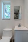 White vanity with a solid-surface countertop and a polished chrome faucet, paired with a frameless rectangular wall mirror, a ceramic toilet, and a wi
