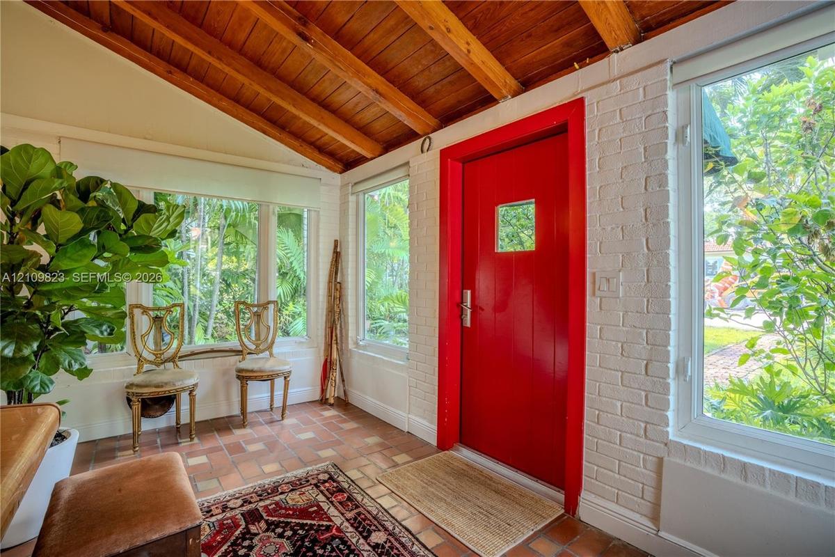 Enclosed porch featuring exposed wood-beam ceiling, white-painted brick walls, tile flooring, and multiple large windows
