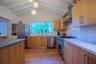 Kitchen featuring vaulted ceilings with exposed beams, light wood-finish cabinetry, stainless steel appliances, and a gas range with a chimney-style v