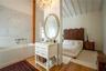 Soaking tub with stone-tiled wall, white vanity with stone countertop, oval wall-mounted mirror, crystal chandelier, and exposed beam vaulted ceiling
