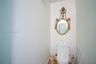 Wall-mounted decorative gold-tone oval mirror featuring ornate detailing and a white high-profile toilet