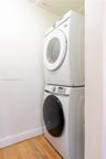Stackable white front-load washer and dryer units situated on wood-finish flooring