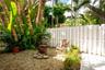 Private outdoor area featuring a gravel surface, perimeter white fencing, and established tropical vegetation