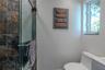 Shower enclosure featuring stone-textured wall tile and a glass door, paired with a white porcelain toilet and a single-pane window