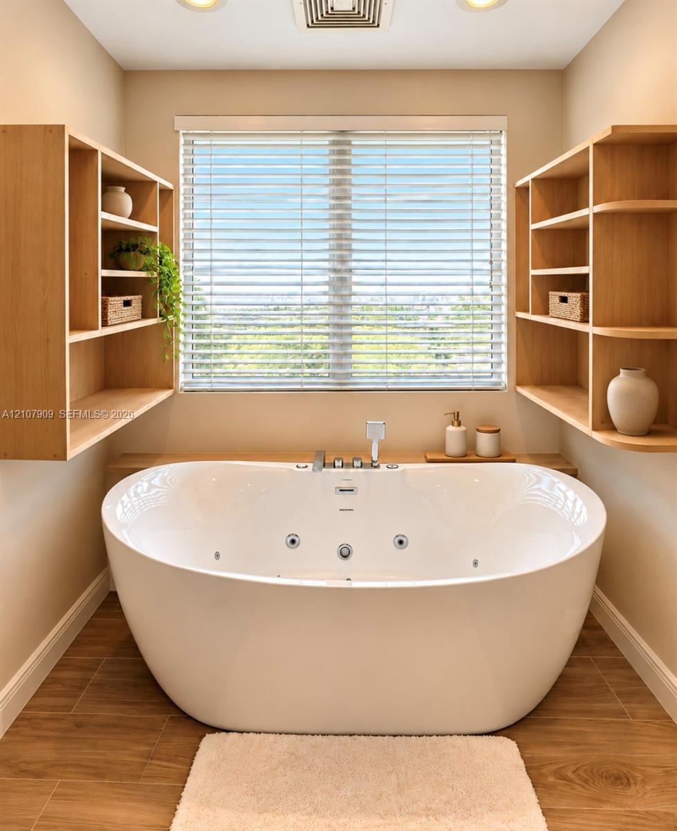 Oval jetted soaking tub with deck-mounted chrome fixtures, flanked by dual light-wood built-in shelving units, finished with wood-finish flooring