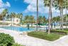 Swimming pool with multi-lane configuration, expansive stone-paver decking, manicured shrubbery, and mature palm trees