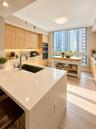 Kitchen featuring light-tone cabinetry, stone-surface countertops, built-in double wall ovens, a deep under-mount sink with a high-arch faucet, and wo