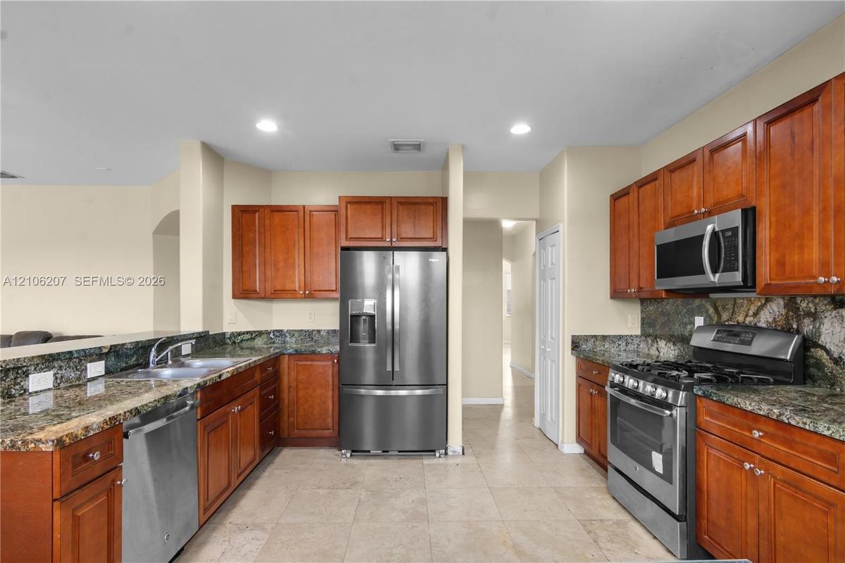 Kitchen featuring medium-tone wood cabinetry, stone countertops, stainless steel appliances, and tile flooring