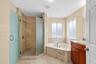 Bathroom featuring a corner soaking tub, walk-in shower with frosted glass enclosure, stone-tile surround, vanity with stone countertop, and an integr