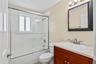 Bathroom featuring a wood-finish vanity with a stone-top integrated sink, a glass-enclosed shower and tub combination with tiled surround, and a wall-
