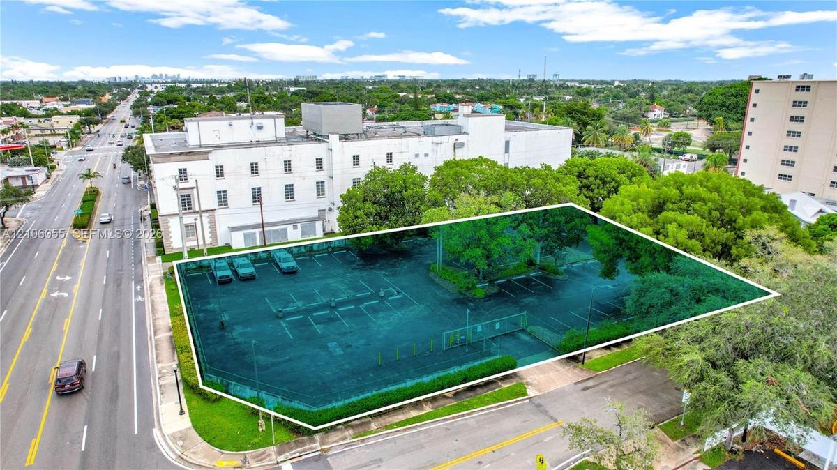Corner lot featuring a paved surface parking area, perimeter landscaping, mature trees, and direct street access