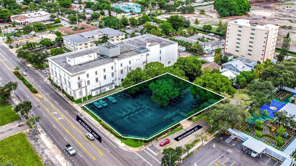 Corner parcel featuring paved surface parking, mature canopy trees, and dual-street frontage at the intersection of N Federal Highway and Buchanan St