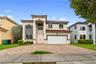 Two-story exterior featuring a clay tile roof, arched entryway, double-door main entrance, and a paved stone driveway with an attached two-car garage