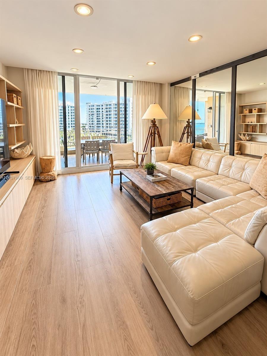 Living area featuring floor-to-ceiling glass sliding doors, wood-finish flooring, built-in light wood cabinetry, recessed lighting, and wall-to-wall m