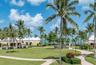 Landscaped grounds featuring mature palm trees, paved walkways, manicured lawn areas, and light-colored exterior structures with gabled roofs