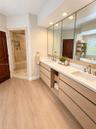 Dual-vanity cabinet featuring light-toned wood cabinetry, stone countertops, integrated under-mount sinks, and widespread faucets, complemented by a w