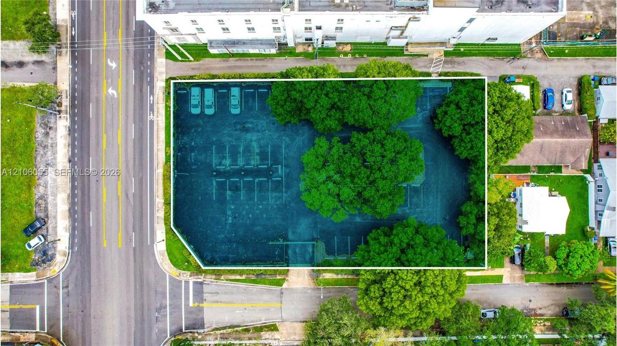 Aerial perspective of a corner lot featuring paved off-street parking, designated parking stalls, and mature trees providing shade